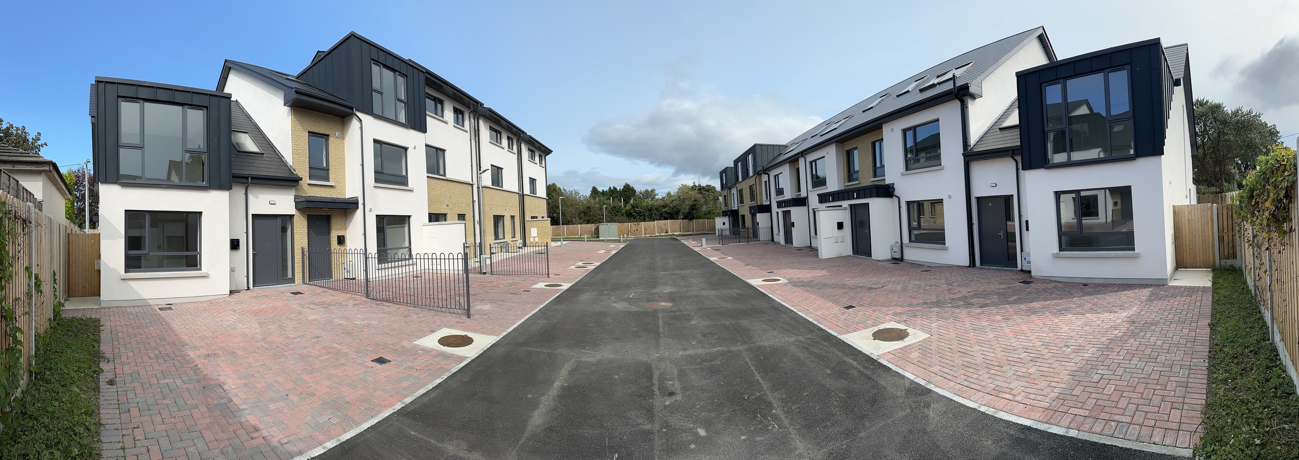 A finished street of new two-storey houses in pale render with dark trim, with fresh paving and kerbs.