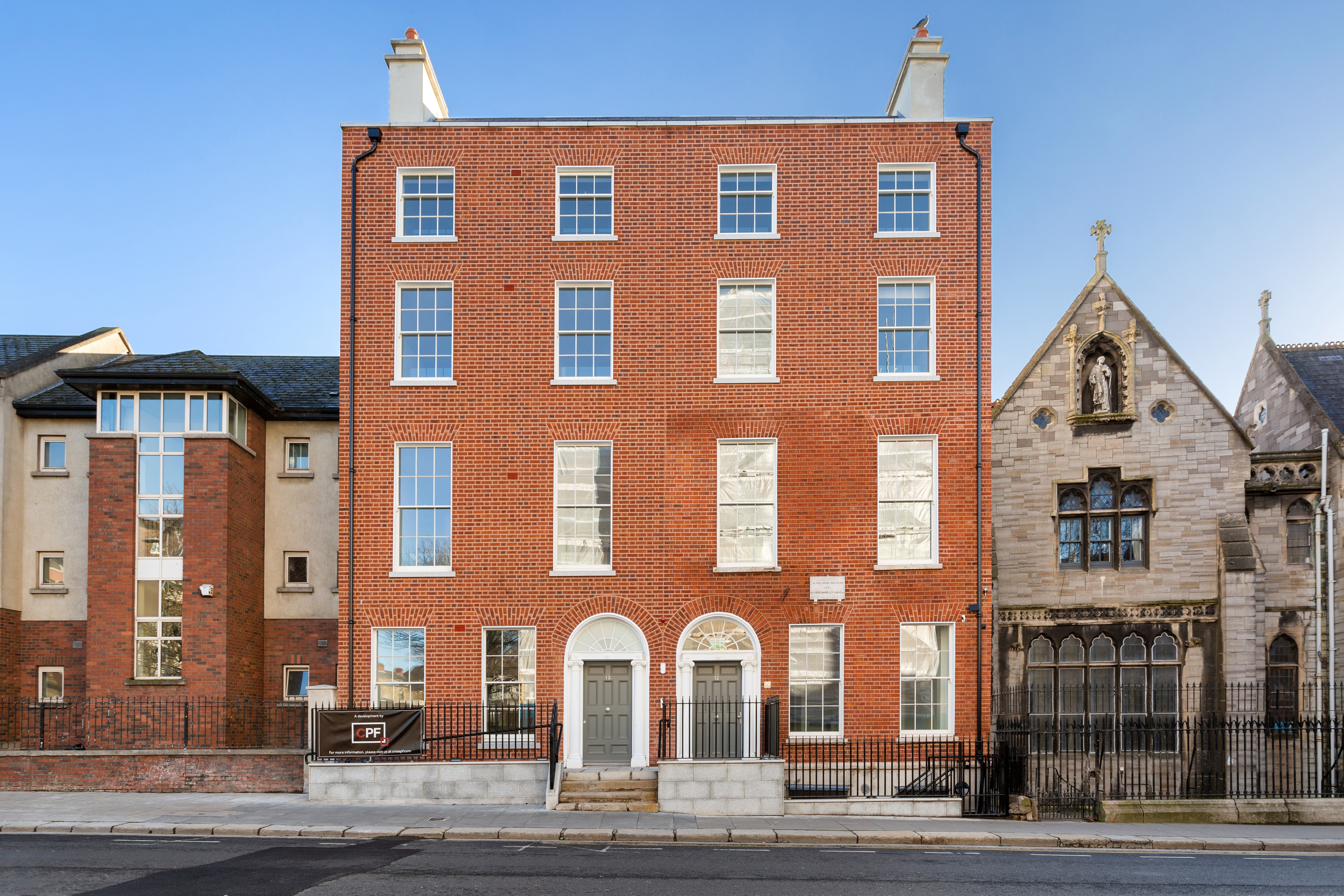 Two red-brick Georgian townhouses on Dorset Street, Dublin, beside a cut-stone church, with cars parked along the kerb.