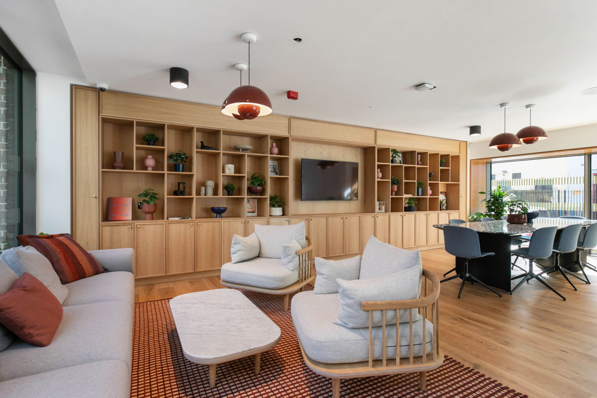 A residents' lounge with built-in bookshelves, pendant lights, sofas and a long shared table.